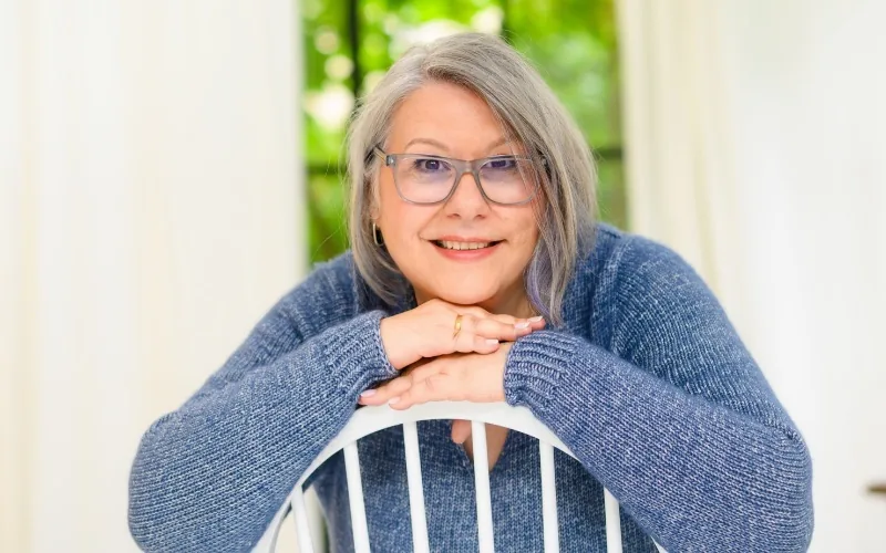 Claudia Eisenkolb, auf eine Stuhllehne gestützt, in einem blauen Strickpullover