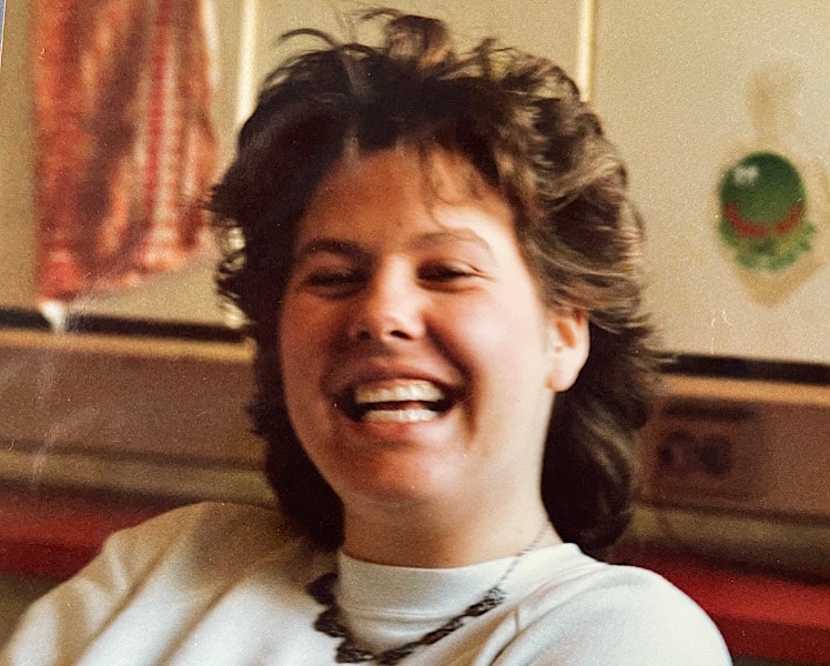 Claudia lachend in hellem Sweatshirt mit Silberkette vor Küchenschränken