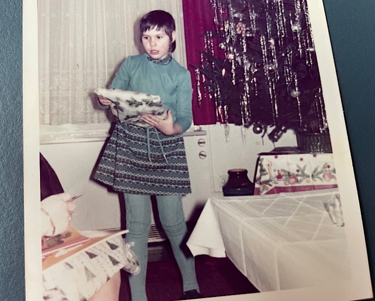 Claudia packt ein Geschenk aus vor einem mit Lametta geschmückten Christbaum
