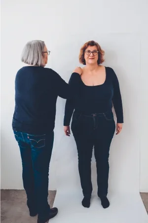 Andrea steht vor einer Wand mit weißem Packpapier und Claudia zeichnet mit einem Bleistift Andreas Umriss