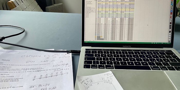 offenes MacBook Pro auf Schreibtisch mit geöffnetem Excel-Sheet zur Berechnung von Größen für ein neues Strickdesign sowie Ausdrucke der Anleitung mit handschriftlichen Notizen