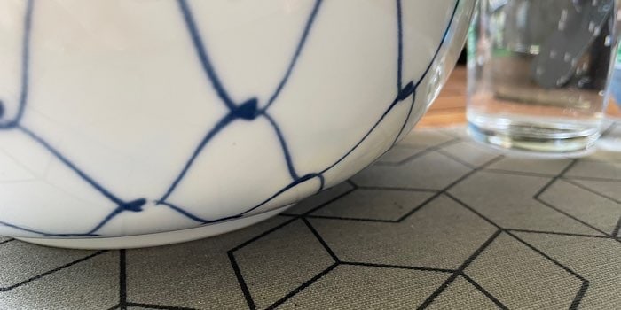 Japanische Schüssel, weiss mit blauem Netzmuster auf einem grauen Tischset mit geometrischem Muster und im mit Wasser gefülltes Glas